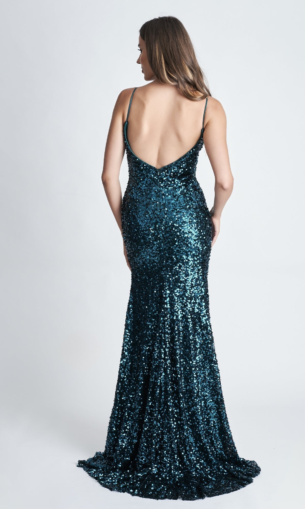 A woman wears the Nina Canacci 4410 long formal dress—a dark blue, sequin, floor-length gown with thin straps, a low-cut back, and a thigh-high slit—posing against a white background.